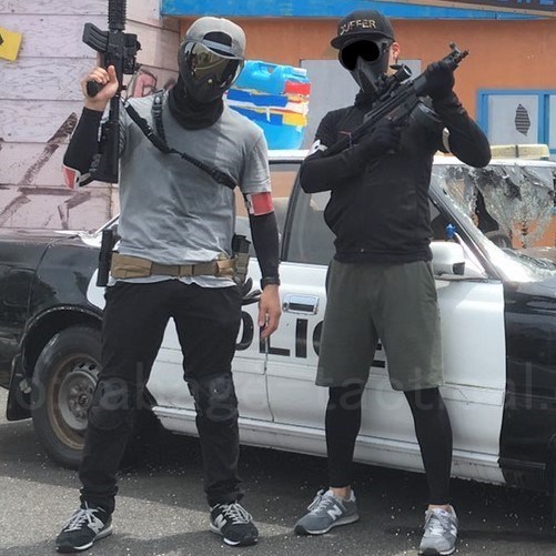 パトカーの前に立つ管理人（左）と友人（右）。管理人は半袖Tシャツの下に黒い長そでのインナー、友人は短パンの下に黒いレギンス