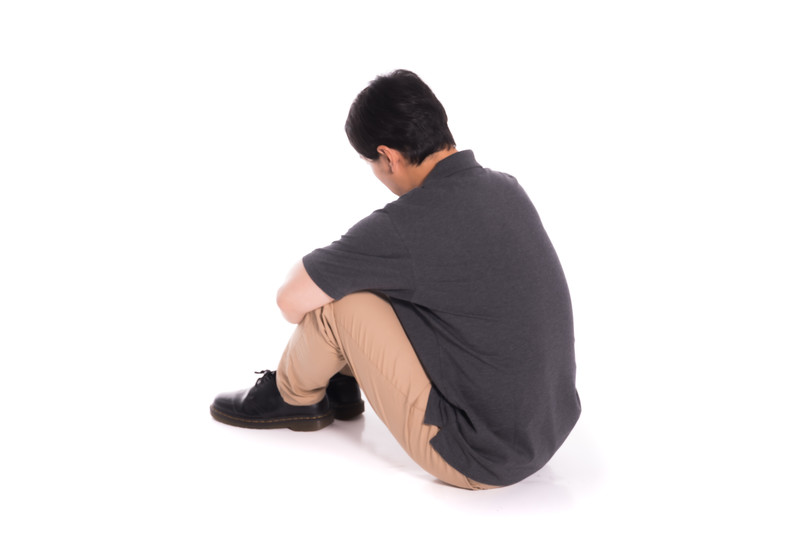 床に座ってひざを抱える男性の後ろ姿