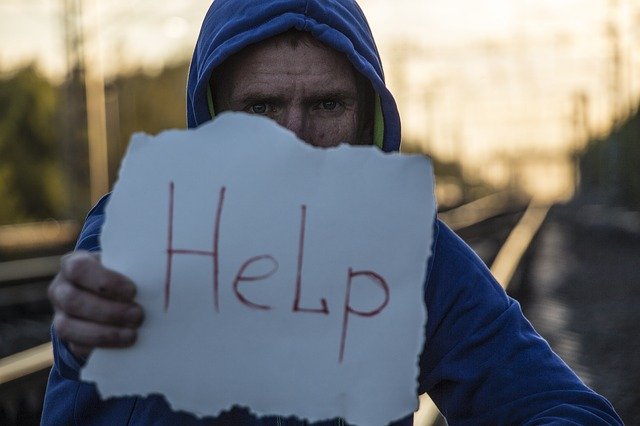 「Help」と書いた紙を持つフードの男性