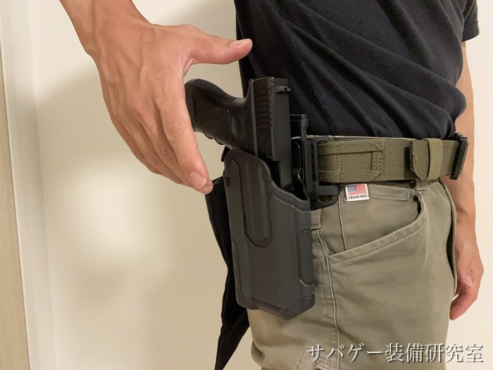 腰のベルトに付けたホルスターにハンドガンを入れるところ