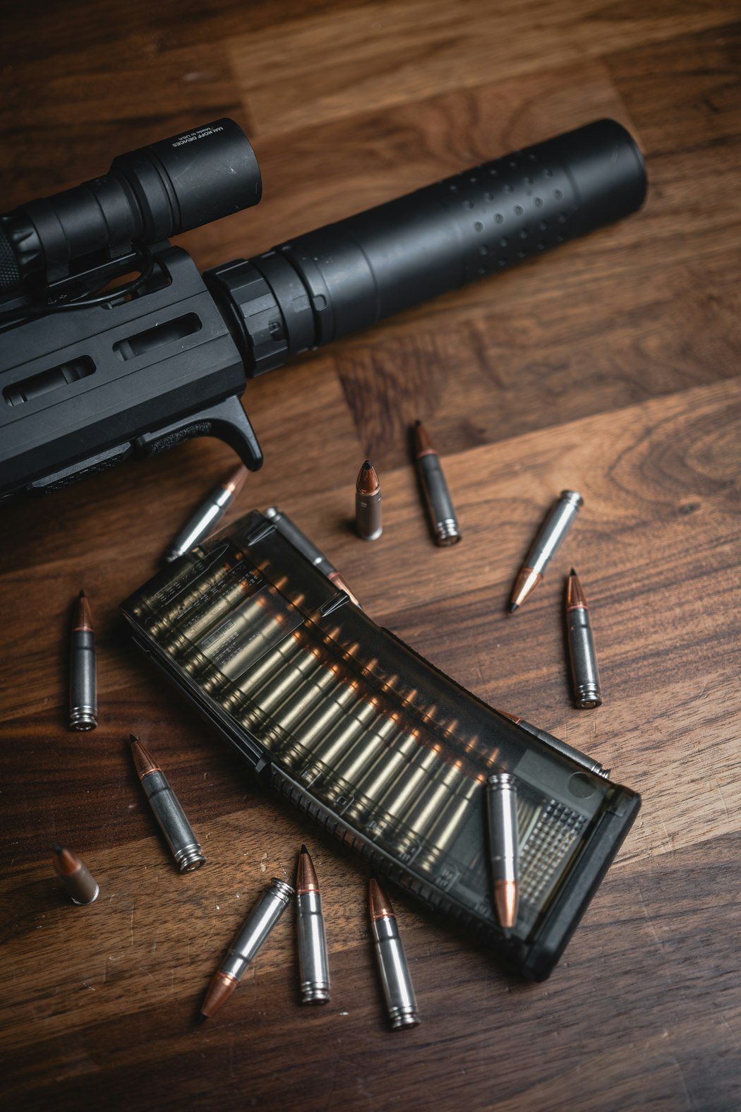 木のテーブルに置いたサプレッサー付きライフルの銃口とマガジン